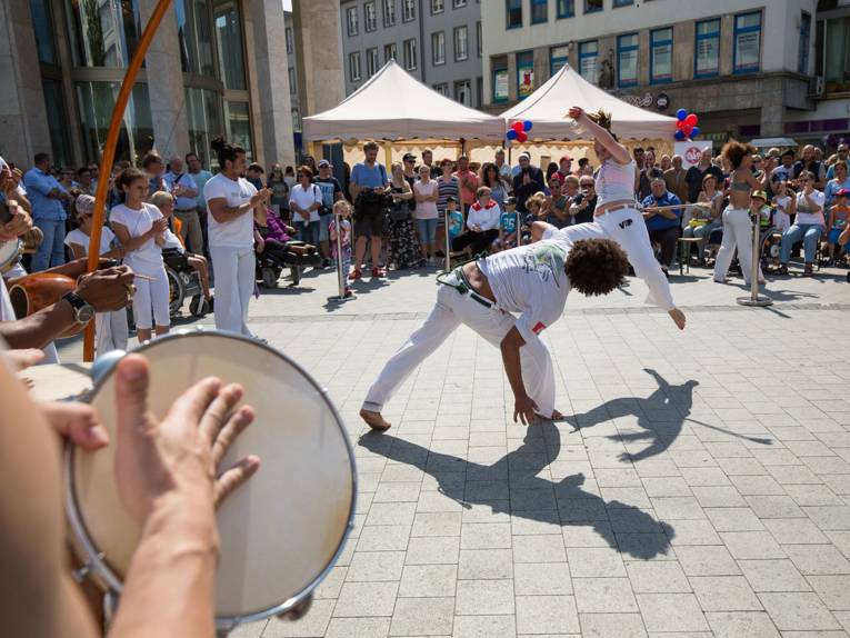 Zwei weiß gekleidete Sportlerinnen wirbeln tanzend-kämpferisch durch die Luft, umringt von Zuschauerinnen und Zuschauern in Hannovers Innenstadt